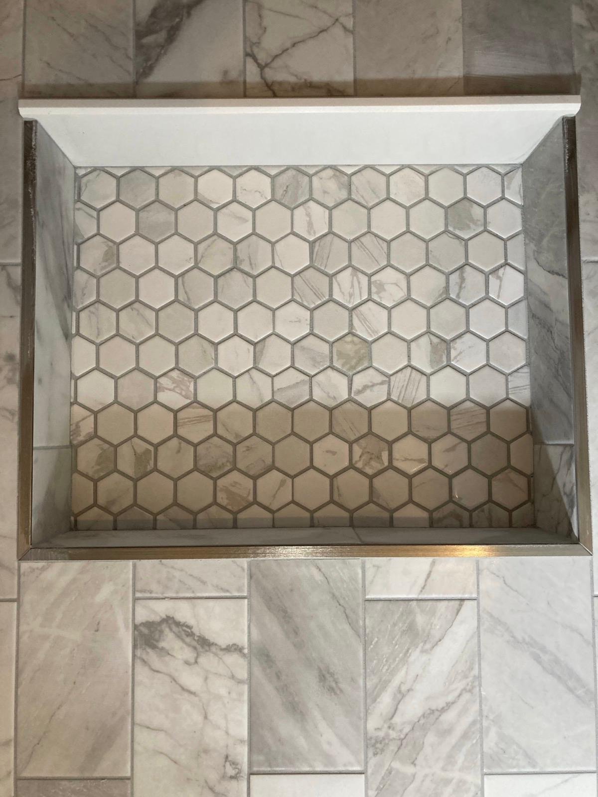 Close-up of marble hexagon mosaic niche set into a wood-grain shower wall