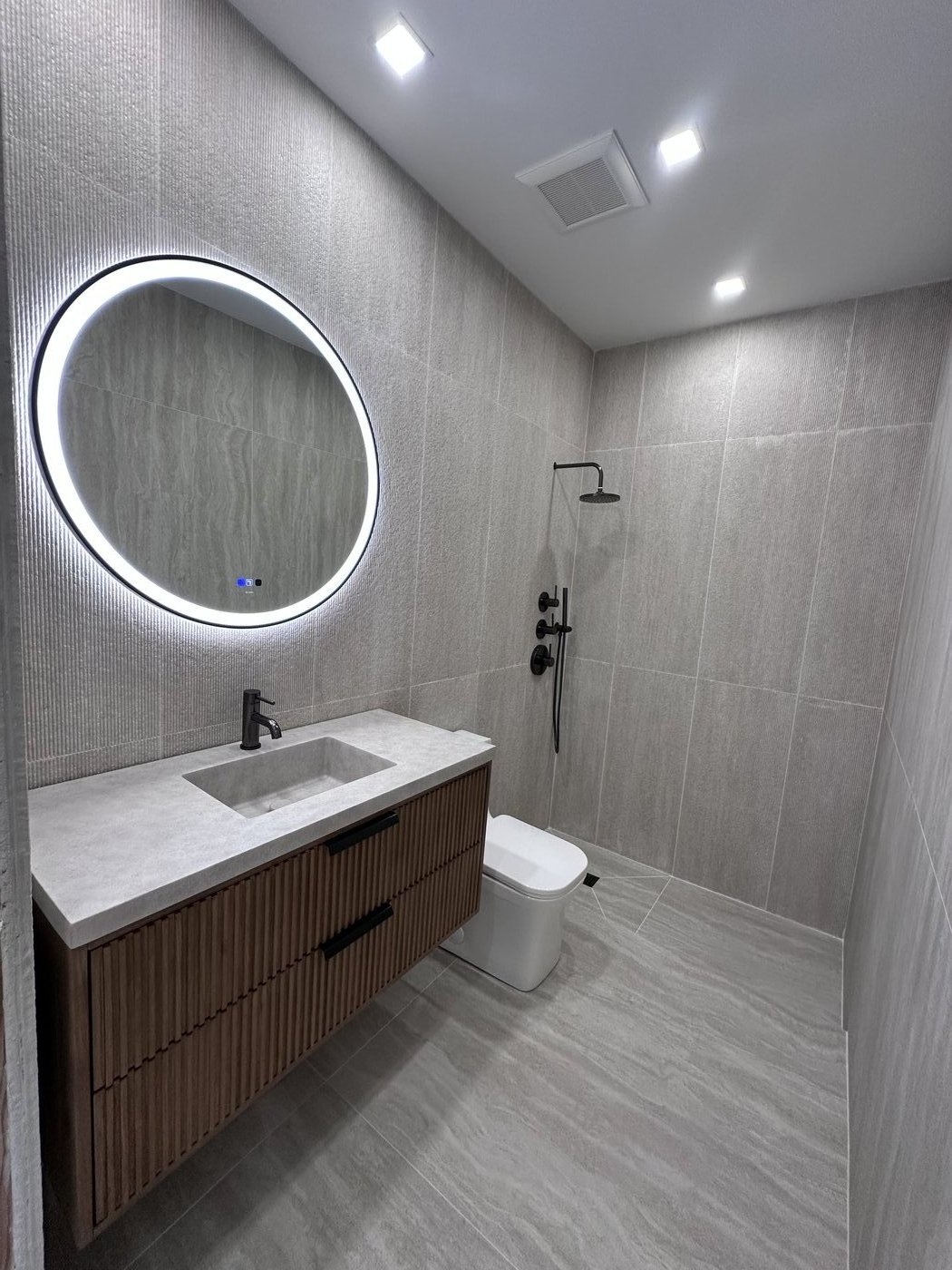 Compact bath with round LED mirror, fluted dark wood vanity and black plumbing fixtures