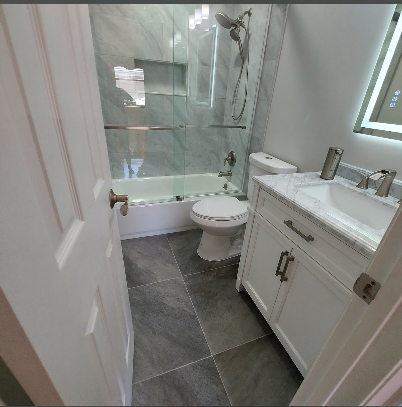 Modern bathroom with marble walls, white shaker vanity and frameless glass shower enclosure