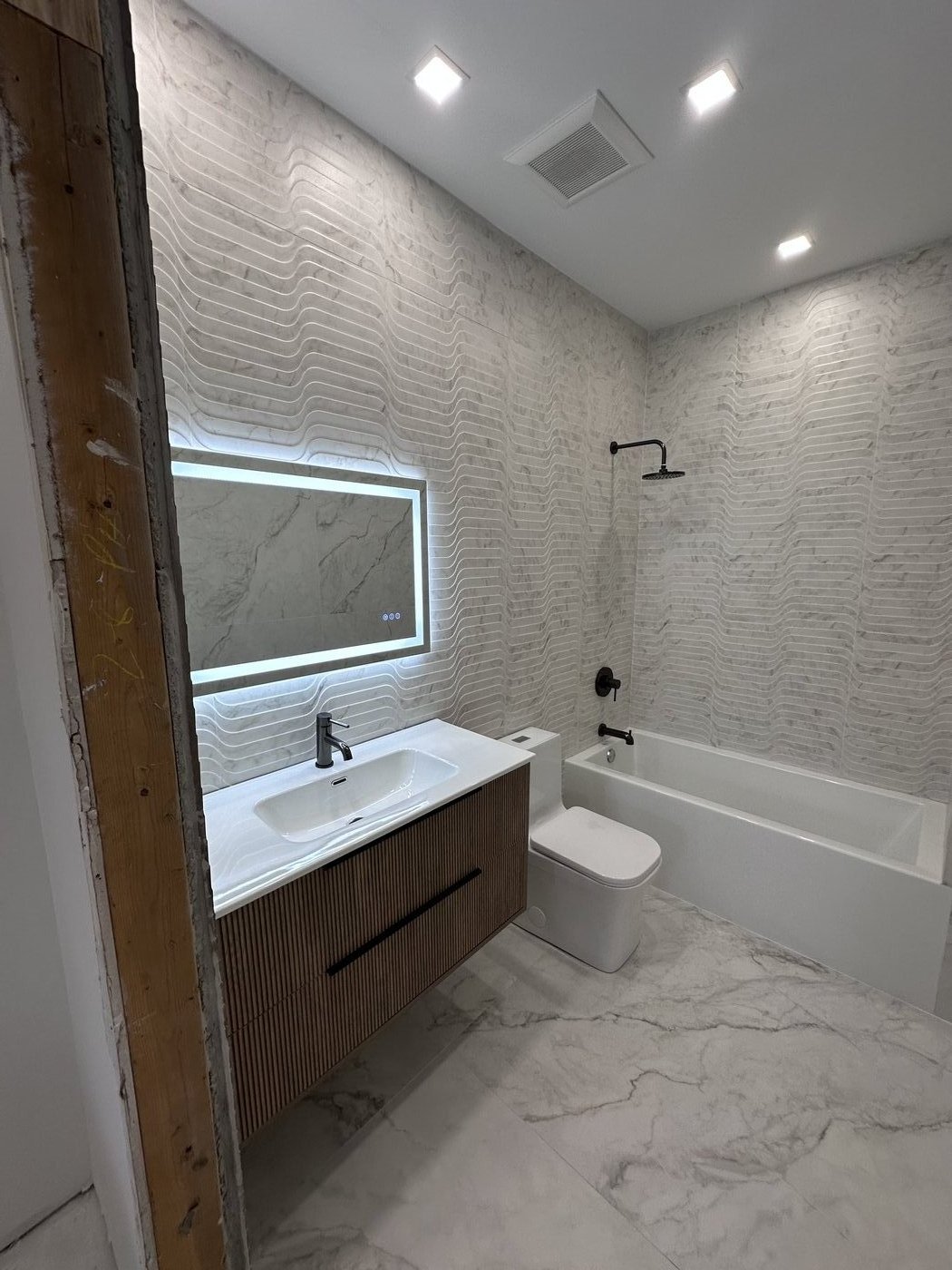 Master bath build with wave-pattern tile, LED mirror, fluted vanity and freestanding tub